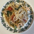 Bord biologische tagliatelle met zalm, spinazie, kerstomaatjes en geraspte kaas, geserveerd op een wit bord met klimopdecoratie.