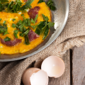 Frittata met Sardijnse venkelworst, gebakken in een pan en gegarneerd met peterselie, geserveerd op rustiek jute met een gebroken eierschaal ernaast.